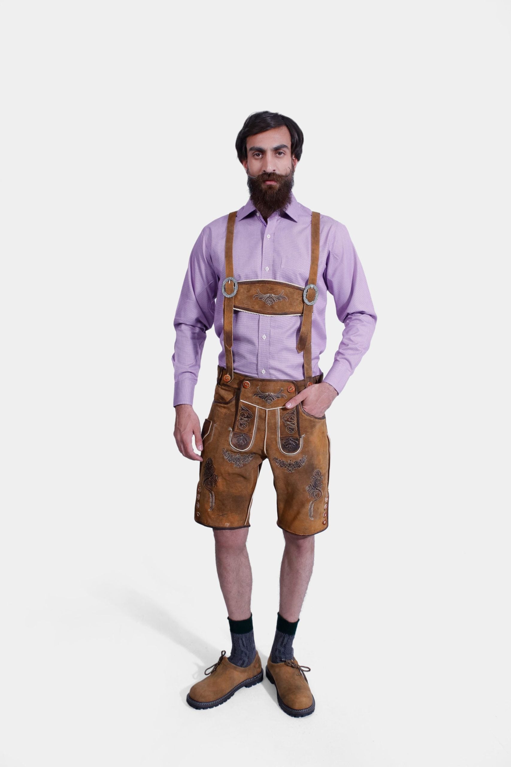 A man wearing traditional Bavarian Lederhosen. He is dressed in a purple long-sleeve shirt and light brown leather shorts with intricate brown embroidery and suspenders. The outfit is completed with dark gray socks and brown shoes, showcasing a classic Bavarian style.