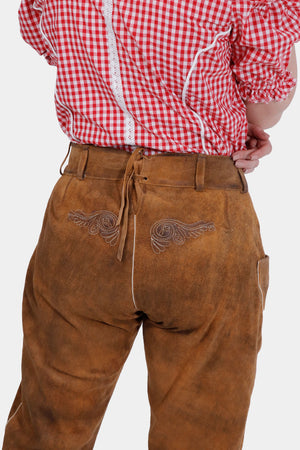 Back view of a woman wearing light brown knee-length Lederhosen with embroidered designs on the back pockets. She is also wearing a red checkered blouse, and her hands rest near her waist.