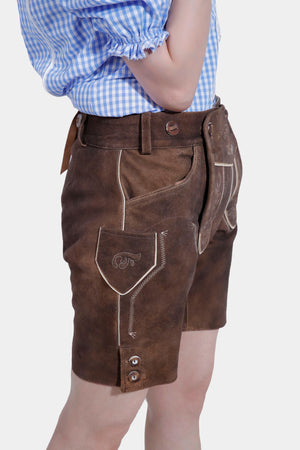 Side view of a woman in a blue and white checkered blouse and brown lederhosen, with her hand in her pocket. The image emphasizes the intricate embroidery on the pocket and side seam of the lederhosen.