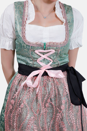 A close-up view of the dirndl, highlighting the intricate pink lace apron and the black ribbon tied at the waist. The woman’s arm is bent, with her hand near her face.
