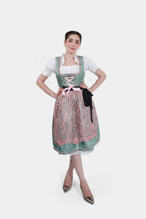 A full-length shot of the woman in the green and pink dirndl, standing with her hands on her hips. She is wearing metallic pointed heels, completing the traditional yet stylish look.