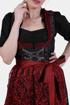 Close-up of the upper half of the dirndl, showcasing the detailed black bodice with red lace trim and a chain across the front, paired with a black blouse.