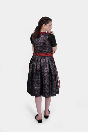 Rear view of the dirndl, showing the black patterned fabric of the skirt and the red lace trim along the back of the bodice.