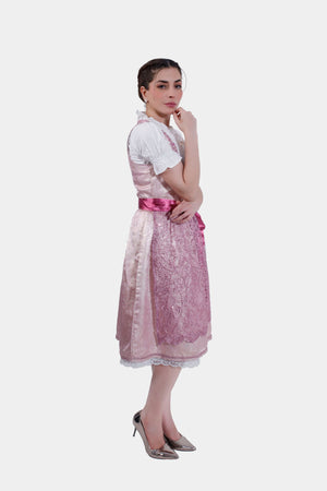 A side profile of the model in the pink dirndl dress, emphasizing the lace apron and the soft sheen of the fabric.