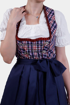 Close-up of the Dirndl dress bodice, showcasing the red and blue plaid pattern, detailed with silver chain accents and a neatly tied navy blue bow at the waist.