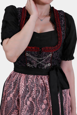 Close-up of the dirndl bodice showcasing detailed embroidery, red lace trim, and silver chain embellishments, paired with a pink lace apron.