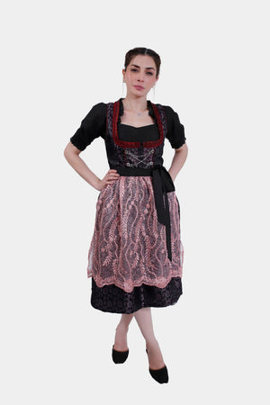 Full-length image of the model in the dirndl dress, featuring a pink lace apron, black floral skirt, and black shoes, with a confident pose.