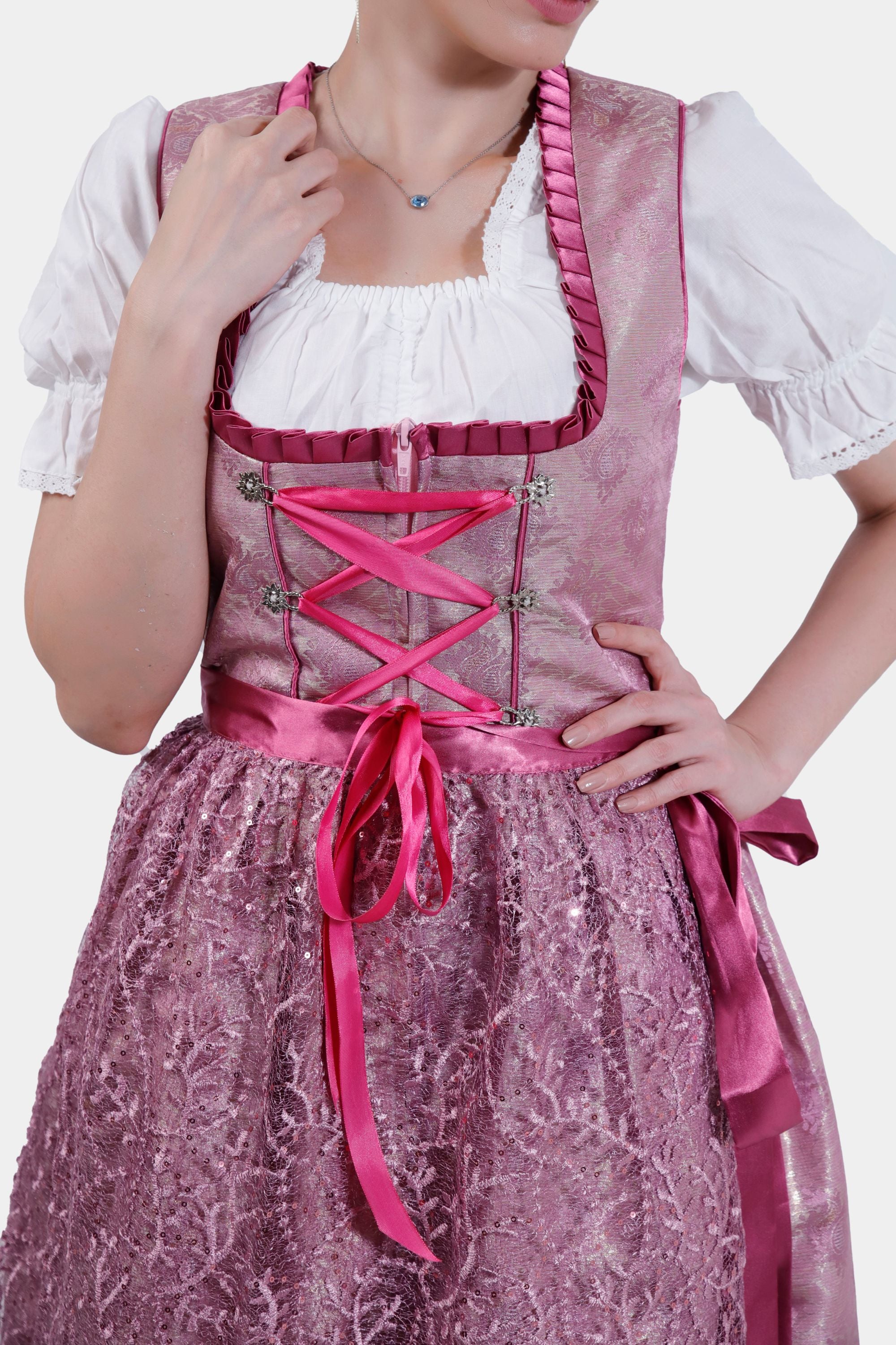 Close-up of the pink dirndl bodice, showcasing the intricate lace details, satin ribbon lacing, and white blouse underneath.