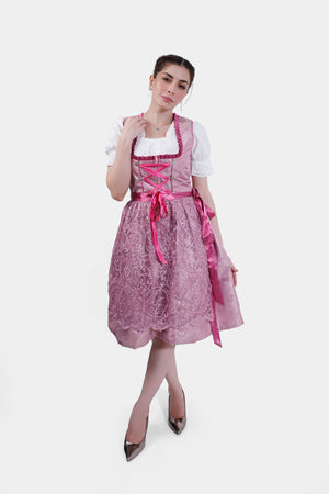 Full front view of a model wearing the pink dirndl, posed with one hand near her neckline, showcasing the entire outfit from top to bottom.