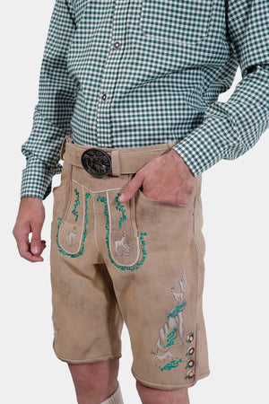 Close-up of a man's waist showing beige lederhosen with green embroidery and a traditional belt buckle, with his hand in the pocket.