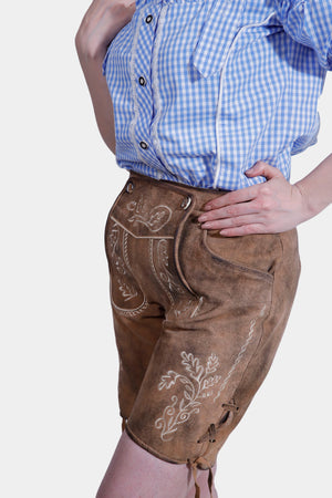 Close-up side view of a person wearing brown lederhosen with white embroidered detailing and a blue checkered blouse.