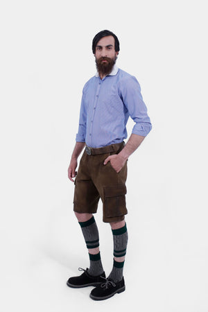 A man in a blue striped shirt is posing in traditional brown leather cargo Lederhosen. The outfit is accessorized with a belt and traditional Bavarian socks and shoes. The side view showcases the side pockets and the decorative belt buckle.