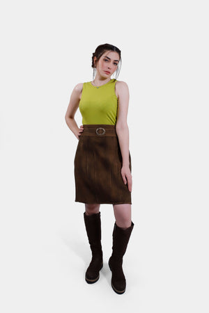 A full-body view of the same woman in the lime green top and brown leather skirt. She is also wearing knee-high brown boots, with one hand on her hip and the other resting by her side, posing confidently against a plain white background.