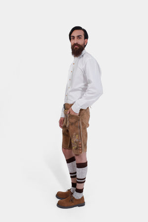 Side view of a bearded man standing confidently in Gerd Muller Lederhosen, complete with knee-high socks and traditional shoes.