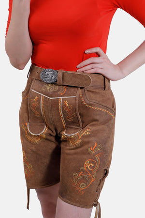 Close-up view of brown leather Lederhosen shorts with intricate floral embroidery in orange and green, paired with a brown belt featuring a silver buckle, worn with a red top.
