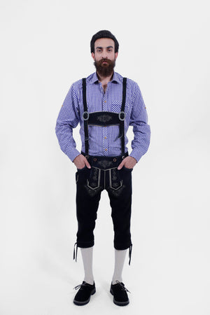 A man wearing traditional Bavarian attire. He is dressed in a purple checkered long-sleeve shirt and black Bundhosen with intricate white embroidery and suspenders. The outfit is completed with cream-colored knee-high socks and black shoes, capturing a classic and elegant Bavarian style.