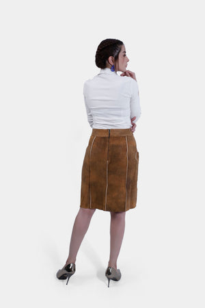 A rear view of a woman wearing a white shirt and a brown leather Jennifer Lederhosen Skirt, showcasing the back design of the skirt, paired with metallic heels.