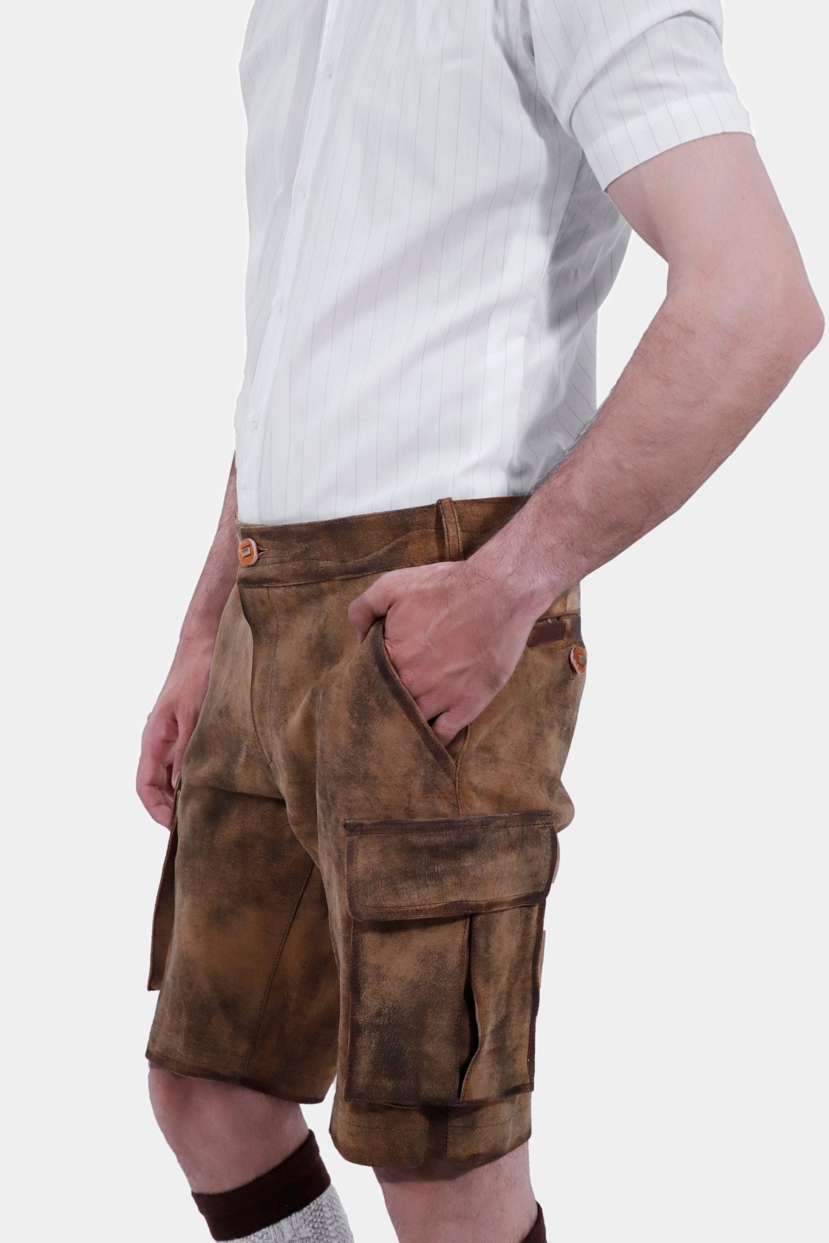 Close-up view focusing on the waist and pocket area of a man wearing brown leather lederhosen and a short-sleeved white shirt. The man has his right hand in the pocket, highlighting the detailed stitching and buttons on the lederhosen.