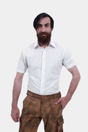 Close-up of a man wearing a short-sleeved white shirt and brown leather lederhosen. The man has his right hand in the pocket of the lederhosen, showcasing the texture and details of the leather shorts and the simple design of the white shirt.