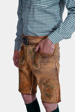 Side view of a man in a Lars Eidinger Lederhosen outfit, showing detailed green embroidery on the tan leather shorts and side laces.