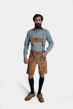 Full view of a man wearing the complete Lars Eidinger Lederhosen outfit, including tan leather shorts with green embroidery, a green checkered shirt, leather suspenders, green knit socks, and brown suede shoes.