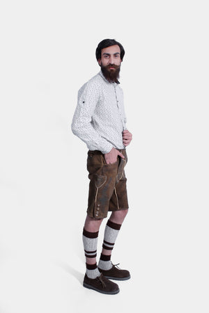 Side view of a man wearing traditional Bavarian Lederhosen. The outfit includes a white shirt with a subtle pattern and brown leather shorts with intricate embroidery. He completes the look with knee-high woolen socks and brown shoes. The attire captures the classic Bavarian style.