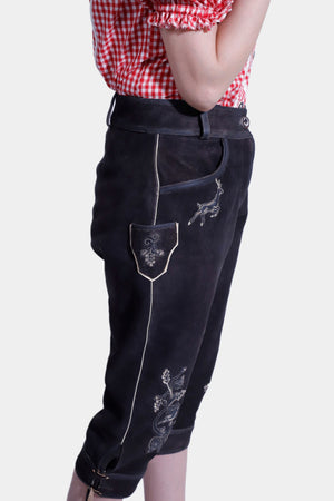 A side profile of the woman showing off the embroidery on the side pocket of her black lederhosen pants. The red and white checkered blouse features puffy sleeves, and the woman has one hand on her waist.