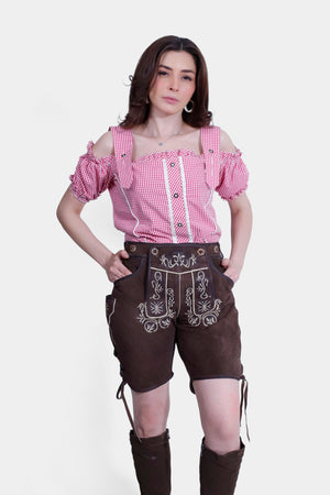 Woman wearing Liesel Pritzker Lederhosen with a green checkered blouse, standing with hands in pockets.