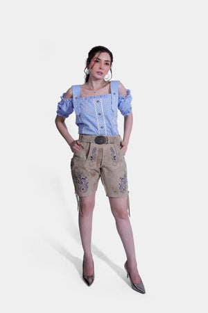 Woman in a blue gingham blouse and tan embroidered leather shorts, standing confidently