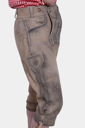 Side view of the woman in a red and white checkered off-shoulder blouse and light brown lederhosen pants, showcasing the intricate embroidery on the side of the pants.