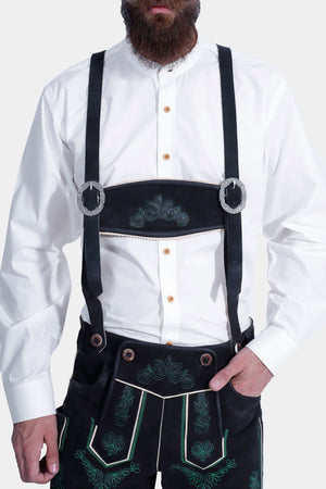 A close-up of the man's torso, focusing on the lederhosen with black suspenders adorned with decorative buckles. The intricate green embroidery on the lederhosen is prominently displayed. He wears a white button-up shirt and stands against a plain white background.