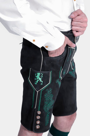 A detailed close-up of the side of the lederhosen, showcasing the intricate green embroidery on the black leather and the side buttons. The man is wearing a white button-up shirt and stands against a plain white background.