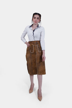 Full body women wearing a traditional brown leather Nena Lederhosen Skirt with white embroidery, buttons, and side pockets, paired with a white blouse with a polka-dotted inner collar