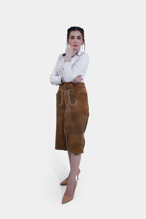 Slightly turned full body view of women wearing a traditional brown leather Nena Lederhosen Skirt with white embroidery, buttons, and side pockets, paired with a white blouse with a polka-dotted inner collar