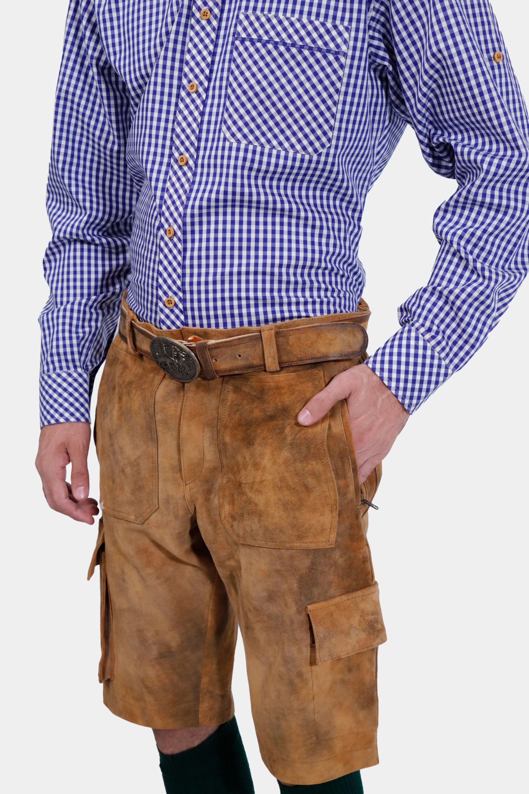 Side profile of a man wearing a blue and white checkered dress shirt and brown cargo lederhosen with pockets. He has his left hand in his pocket and is looking slightly towards the camera.