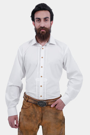 A man with a beard is wearing traditional light brown leather Lederhosen paired with a white shirt. The Lederhosen are knee-length and feature intricate embroidery. The outfit is completed with traditional Bavarian socks and brown shoes.