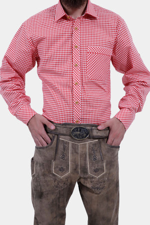 Close-up view of a man wearing a red and white checkered shirt, showcasing the detailed buttons and front pocket. He is also wearing light brown leather bundhosen with an ornate belt buckle, his hands resting on his hips.
