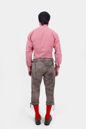 Rear view of a man wearing a red and white checkered shirt and light brown leather bundhosen, showing the back pockets and overall fit of the bundhosen along with bright red knee-high socks.