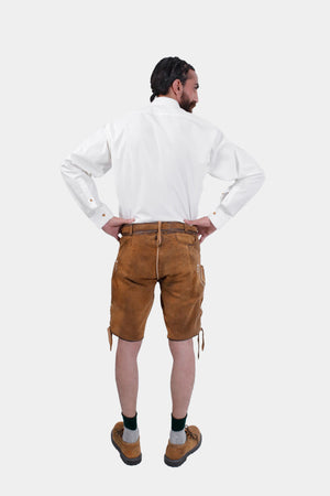 Back view of a man wearing a white dress shirt and brown lederhosen. The back of the lederhosen is plain compared to the front, and he has his hands on his hips.