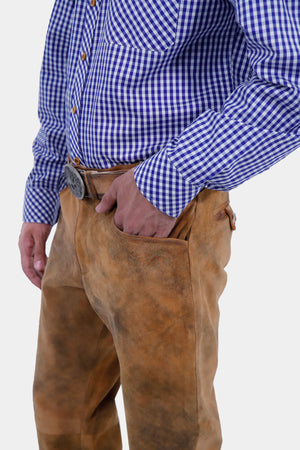 Side view of a man wearing a blue and white checkered shirt and brown leather long lederhosen. His hand is in his pocket, emphasizing the decorative stitching and unique pocket design on the lederhosen.