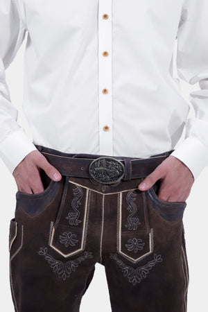 Close-up view of a man wearing dark brown leather Bundhosen with a decorative belt buckle, highlighting the detailed embroidery on the front. The man is also wearing a white button-up shirt