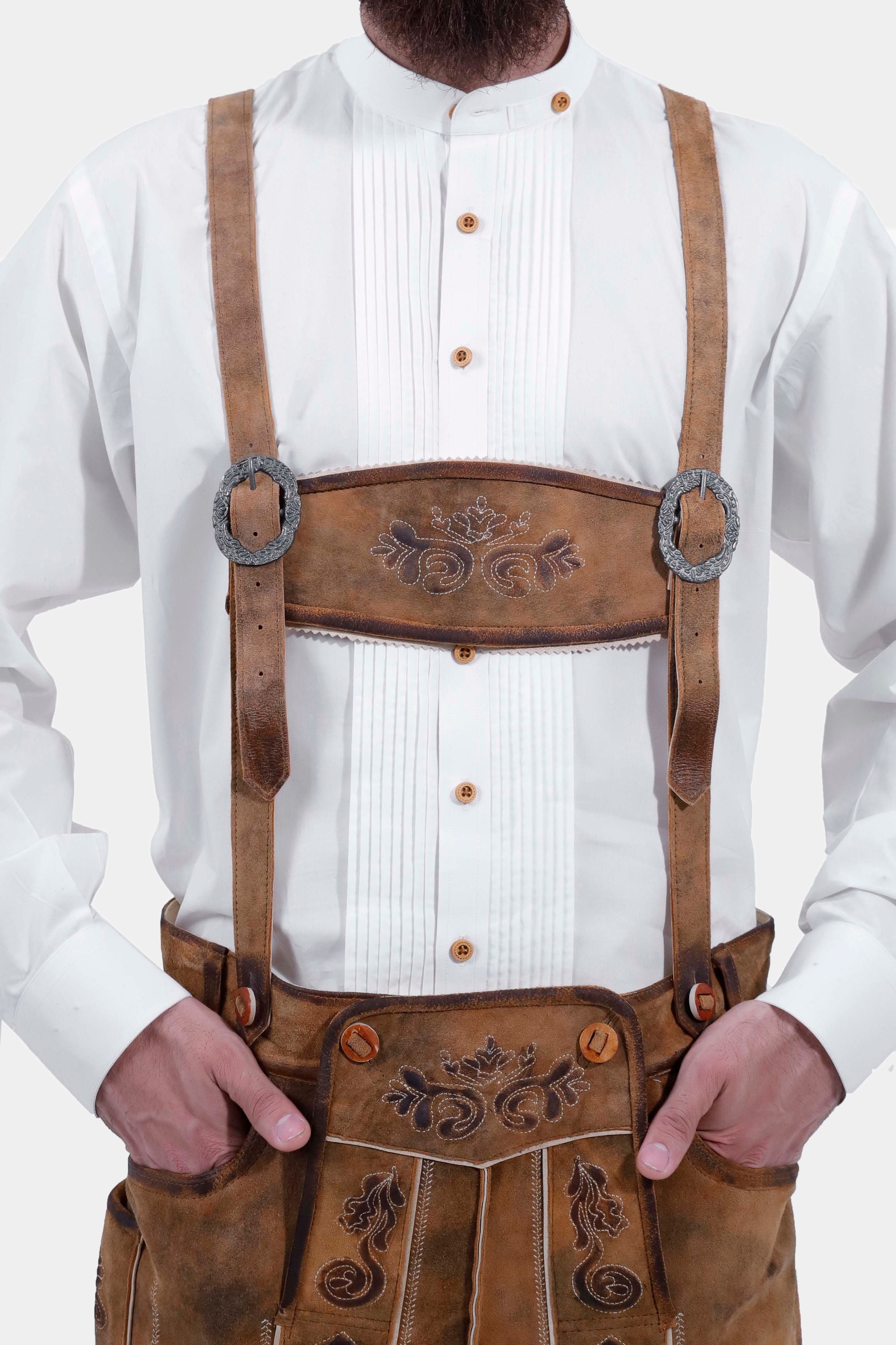 Close-up view of a man wearing brown leather Bundhosen with a decorative traditional suspender, highlighting the detailed embroidery on the front. The man is also wearing a white button-up shirt.