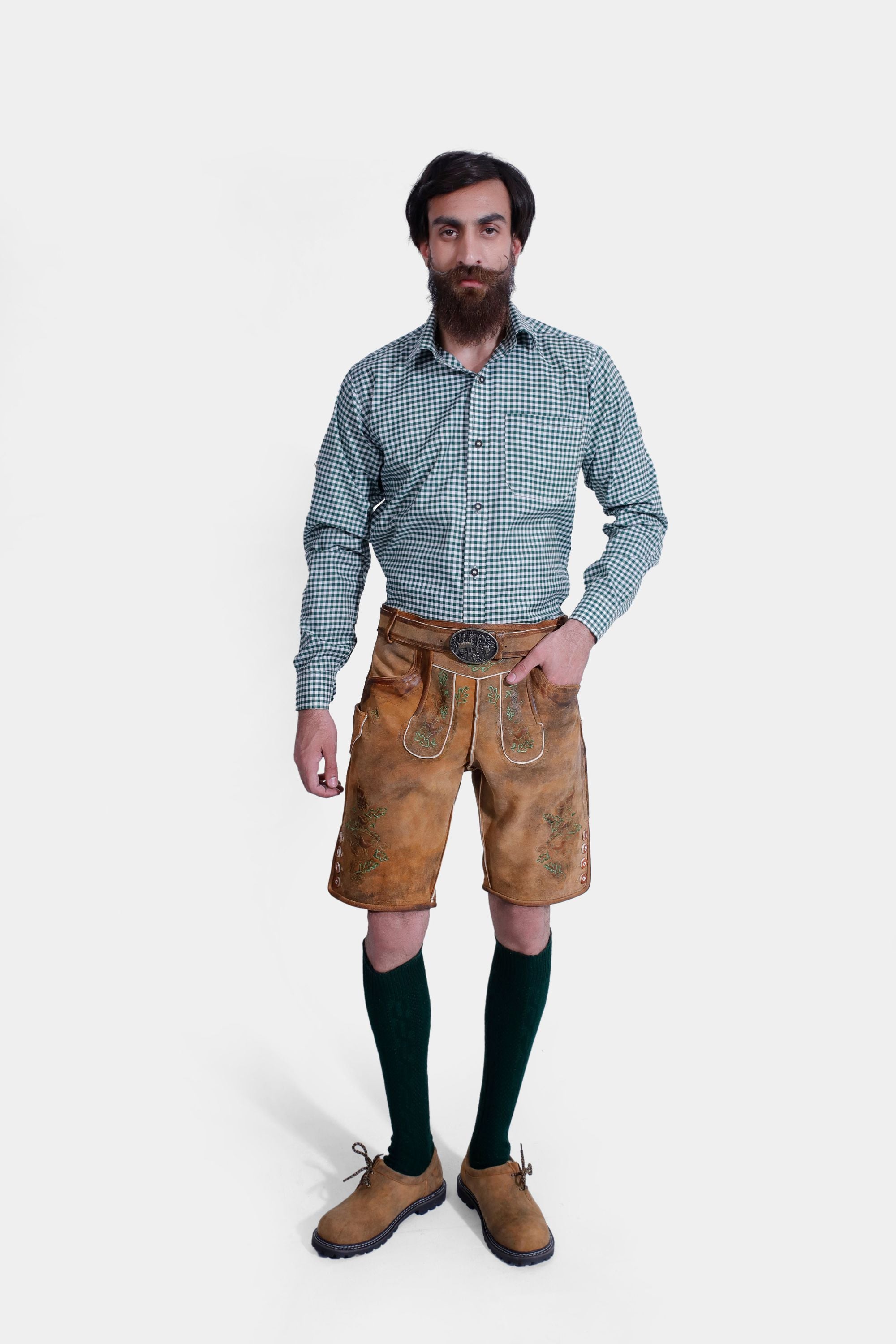 The same man standing in a relaxed pose, showcasing his full outfit, which includes green knee-high socks and brown shoes. The lederhosen's detailed embroidery and buttons on the side are clearly visible.