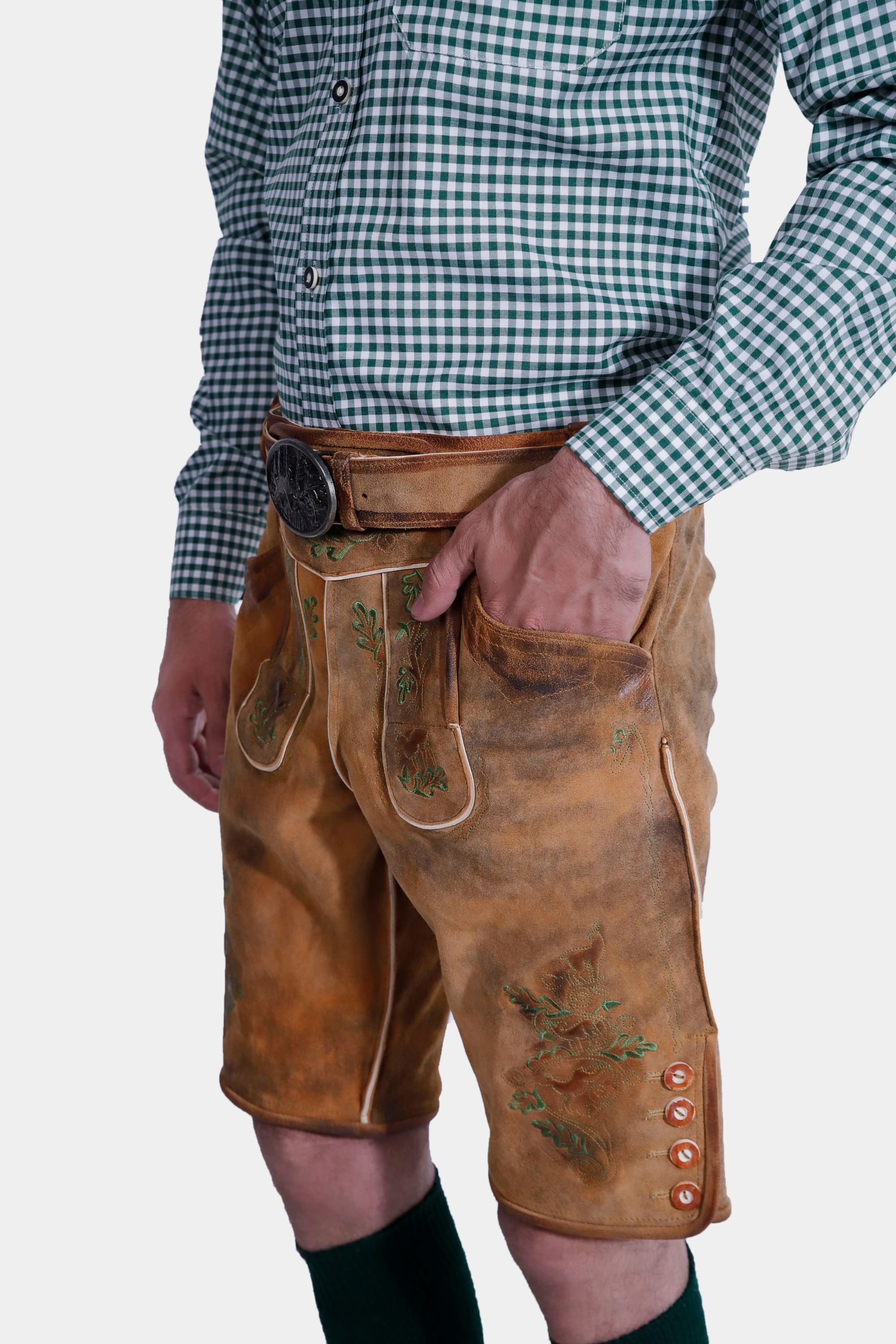 A close-up view focusing on the man's upper body, highlighting the green embroidered suspenders attached to the lederhosen. The suspenders feature metal buckles and are worn over the checkered shirt.