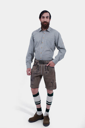 A man wearing earthy brown leather Bavarian Glory Suspenders with intricate embroidery and circular metal clasps, paired with a green checkered shirt, matching Bavarian Woodland Lederhosen, green and cream knee-high socks, and brown shoes.