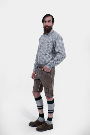 Another side view of the man wearing the green checkered shirt and brown Lederhosen. The detailed embroidery on the Lederhosen is visible, and the man has his hand in his pocket.