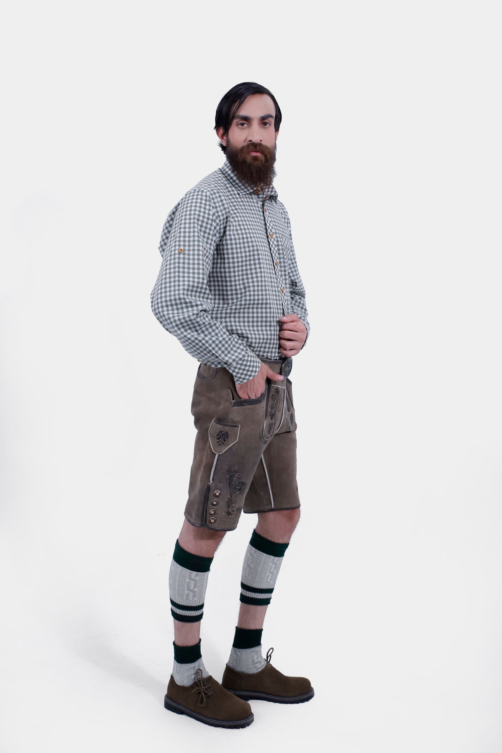 Side view of the man wearing the green checkered shirt and brown Lederhosen. The detailed embroidery on the Lederhosen is visible, and the man has his hand in his pocket.