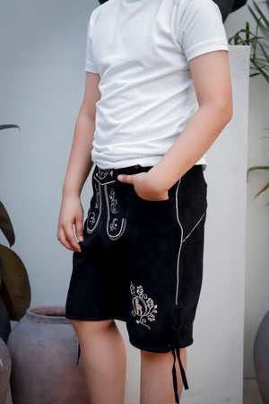 Side view of a young boy in a white t-shirt wearing 'Bernd Leno Lederhosen' in black, highlighting the intricate white embroidery and lace-up detail on the legs.