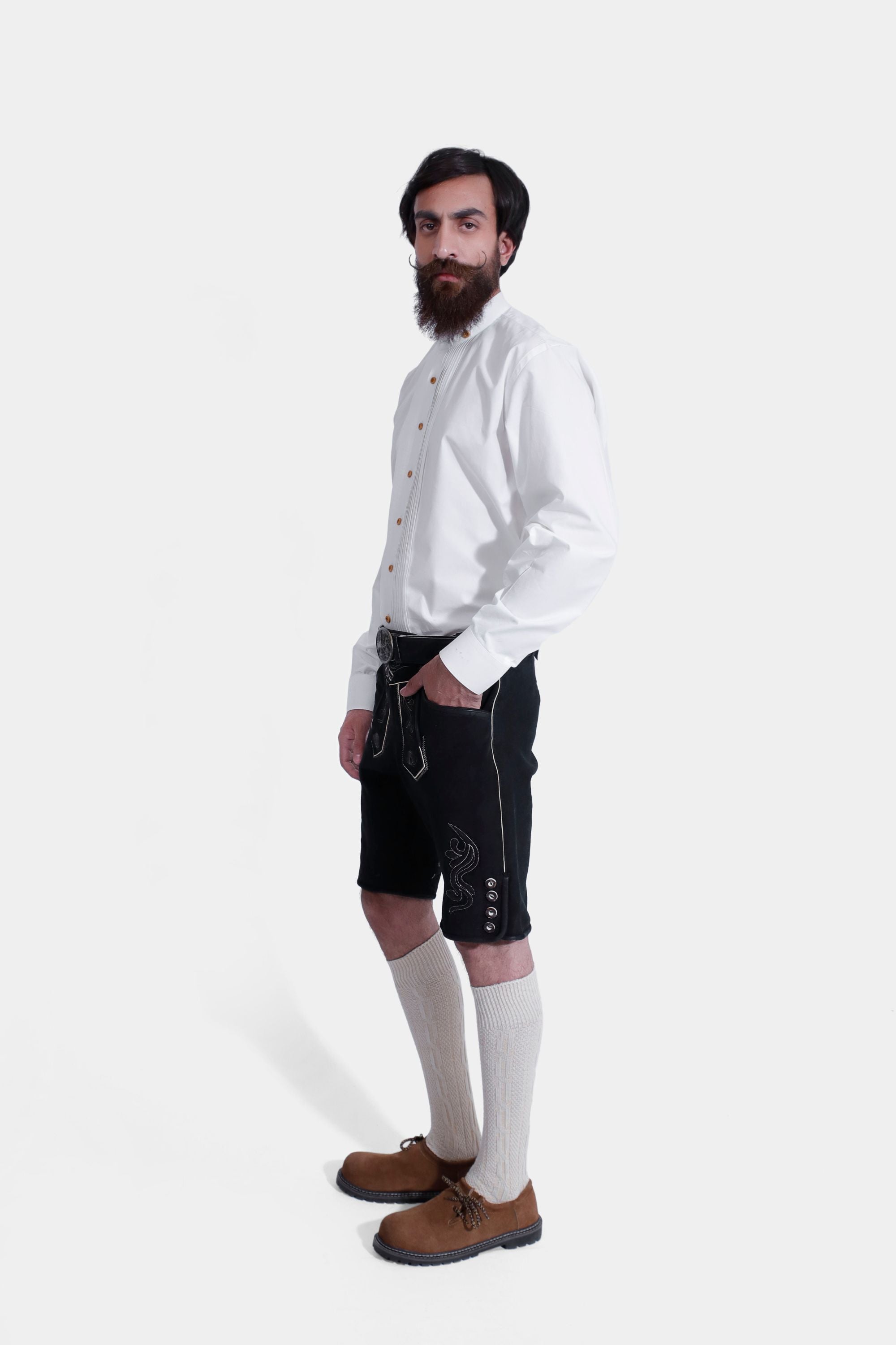 Side view of a man wearing Black Edelweiss Lederhosen in Obsidian Twilight with natural embroidery, white shirt, and traditional knee-high socks.