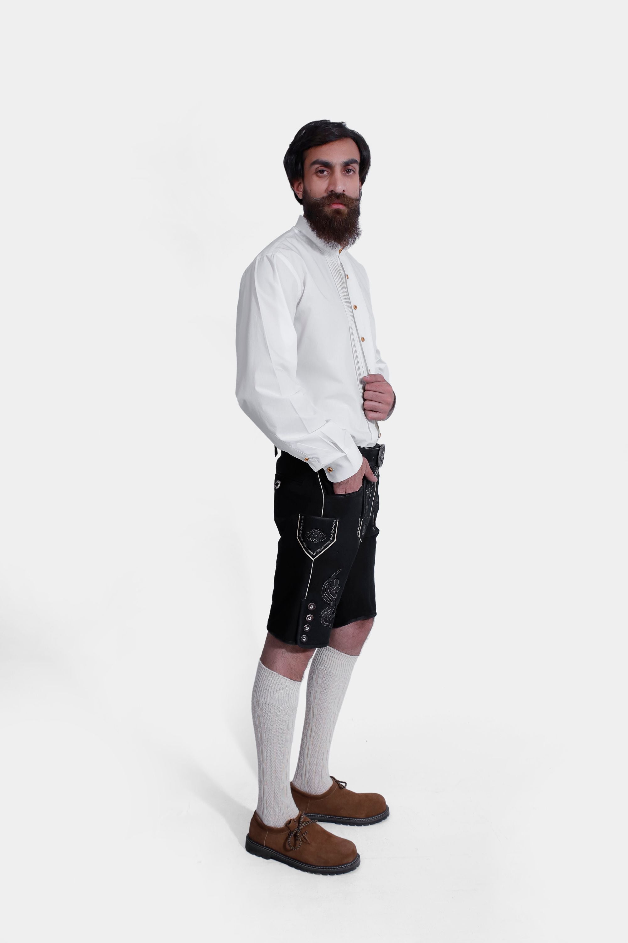 Side view of a man wearing Black Edelweiss Lederhosen in Obsidian Twilight with natural embroidery, white shirt, and traditional knee-high socks.